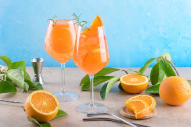 Classic italian aperitif aperol spritz cocktail in two wineglasses with ice cubes and slice of orange with light blue background on beige stone background, traditional summer fresh iced drink, closeup