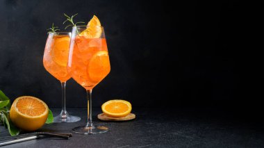 Classic italian aperitif aperol spritz cocktail in two wineglasses with ice cubes and slice of orange on black stone background, traditional summer fresh iced drink, closeup, copy space, banner