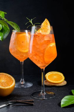 Classic italian aperitif aperol spritz cocktail in two wineglasses with ice cubes and slice of orange on black stone background, traditional summer fresh iced drink, closeup
