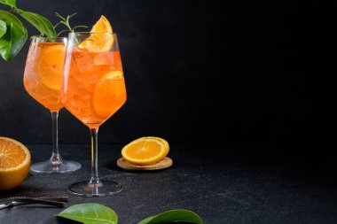Classic italian aperitif aperol spritz cocktail in two wineglasses with ice cubes and slice of orange on black stone background, traditional summer fresh iced drink, closeup, copy space