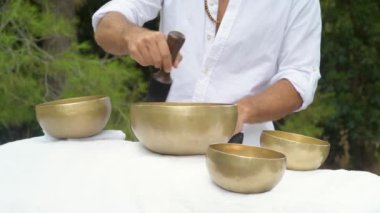 Beyazlı bir adam Tibet şarkı kasesiyle ses masajı yapıyor. Şifa veren ses terapisi sırasında tahta bir çubuğu kasenin kenarına taşıyor.