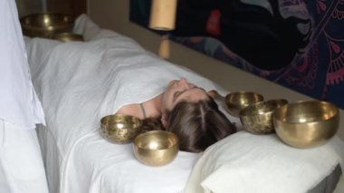 Beyazlı bir adam, ses iyileştirme terapisi sırasında bambu Koshi çan müzik aleti kullanıyor. Genç bir kadının üzerinde Tibet müzik kaseleri var. Kapalı alanda masaj yaparken, seçici bir odak noktası.