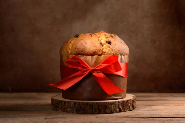 Geleneksel İtalyan Noel Keki Panettone, ahşap arka planda kırmızı fiyonklu. Ev yapımı ekşi mayalı panettone yemek için hazır. Klasik İtalyan Noel Yemeği ve Yenilebilir Hediye