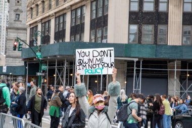 A young Female holding a cardboard sign with the words You Don't Owe me I'm not your policy  written on it a