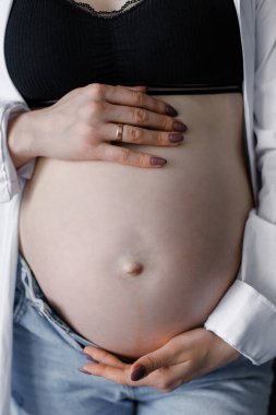 a pregnant girl holds her stomach from above and below with both hands. Close-up photo. Woman in bra and jeans and shirt