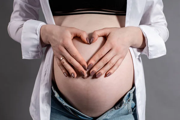 a pregnant woman in the seventh month of pregnancy holds her hands on her stomach, folding them in the shape of a heart. close up photo
