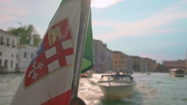 Italiensk sjöflagga viftar på båtfärd, Canal Grande, Venedig, Italien, på dagen. Medeltida byggnader och taxibåt i bakgrunden, selektivt fokus — Stockvideo