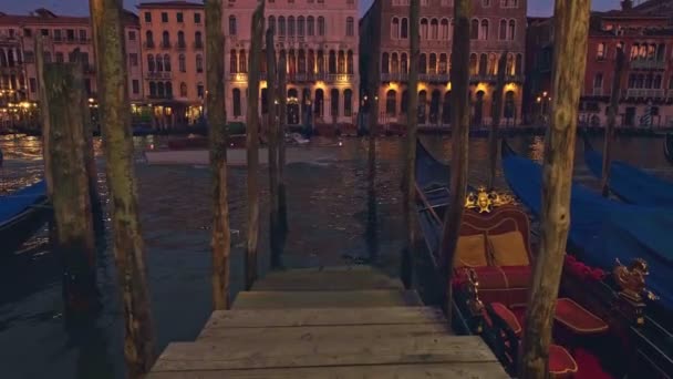 Γόνδολες επιπλέουν στα νερά του Μεγάλου Καναλιού στη Βενετία της Ιταλίας, τη νύχτα. Μετωπική λήψη σταθμευμένων σκαφών με μπλε καλύμματα, μεσαιωνικά κτίρια στο παρασκήνιο — Αρχείο Βίντεο