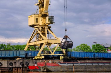 Bulutlu bir günde rıhtımda demirli nehir iskele vinci ya da nehir sürükleme botlarına kömür yükleyen mızraklı vinç. Enerji, mineraller, çevre 