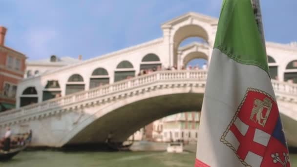 Italiensk sjöflagga viftar under båtfärd på Canal Grande, Venedig, Italien, på dagen. Rialtobron eller Ponte di Rialto i bakgrunden, selektivt fokus — Stockvideo