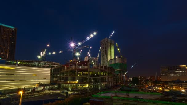 Nachtelijke tijdspanne van de bouwplaats. Veel kranen bewegen, hoge gebouwen in het midden van de moderne stad, heldere lichten. Verstedelijking, ontwikkeling — Stockvideo