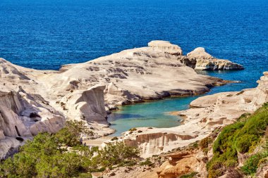 Sarakiniko sahilinin ünlü beyaz kayaları, Ege Denizi, Milos Adası, Yunanistan. Çok az turist gölgede saklanır, boş uçurumlar, yaz güneşi, berrak deniz, mavi sular, güzel manzara, fantastik kayalar
