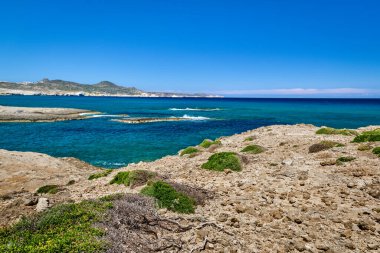 Güneşli bir yaz gününde Yunan adasının tipik güzel manzarası. Büyük mavi gökyüzü ve bulutlar, kayalık uçurumlar, küçük yeşillikler. Milos Adası, Yunanistan