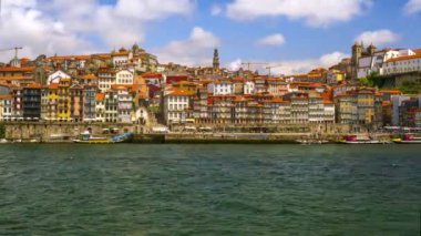 Day time lapse of clouds fly above Portos oldest district Ribeira by Douro river, Portugal. People rush around embankment, tourist boats rush up and down, river taxi crossing Douro. Summer sunshine