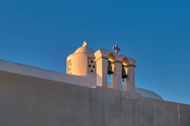 Beyazlatılmış Yunan Ortodoks kilisesi, haçlı ve zilli küçük çan kubbesi, gün batımında gökyüzü arka planında çatı ve kubbe. Hıristiyanlık, din, gelenekler, semboller, mimari. Yakın çekim. Milos Adası, Yunanistan