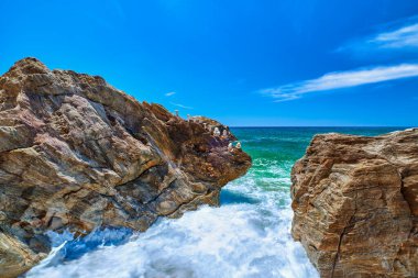 Deniz dalgaları güneşli yaz gününde kayaları dövüyor, açık gökyüzü, uzun pozlama. Kayanın kenarındaki küçük denge taşı yığını. Gök mavisi sular, beyaz deniz spreyi. Mükemmel deniz manzarası, tatil yerleri. Paleochori