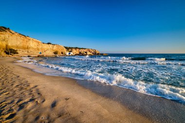 Yunanistan 'ın Milos adasındaki Fyriplaka plajının güzel günbatımı manzarası. Yunan tatilleri, Ege denizi, yüksek kayalık manzaralar, gök mavisi sular, kumlu plaj, insan yok, geleneksel turistlerin eşsiz yerleri