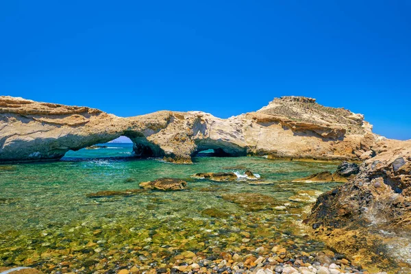 Sunny landscape of rocky small bay with azure clear sea waters, islet caves, stone arches. Mediterranean vacation, summer holiday, sunny summer day, swimming. Great blue sky, no clouds, rocky cliffs