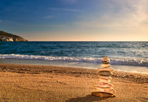 Small balance stone stack or cairn on sandy beach in sunset sunlight, sea waves. . Tidal waves in background, selective focus, blurred background, colorful view. Concept of balance, meditation, peach