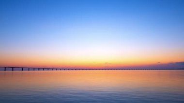 Tagus ya da Tejo nehri ve Lizbon, Portekiz 'deki Vasco da Gama köprüsü üzerinde renkli gündoğumu zamanı. Vasco da Gama köprüsünün üzerinde yükselen güneşe doğru zum yapıyor ve arabalar oradan geçiyor. Sakin nehir akıntısı