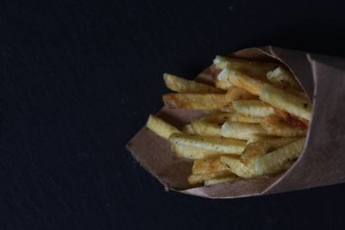 fast food concept - paper cone of french fries isolated on dark background flat lay. Image contains copy space
