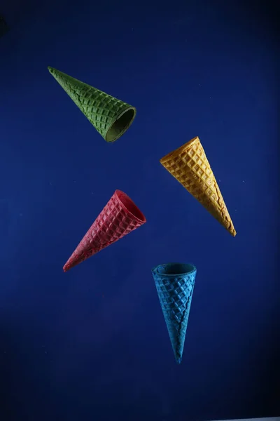 四个不同颜色的华夫饼圆锥在蓝色背景下飘扬 图像包含复制空间 — 图库照片