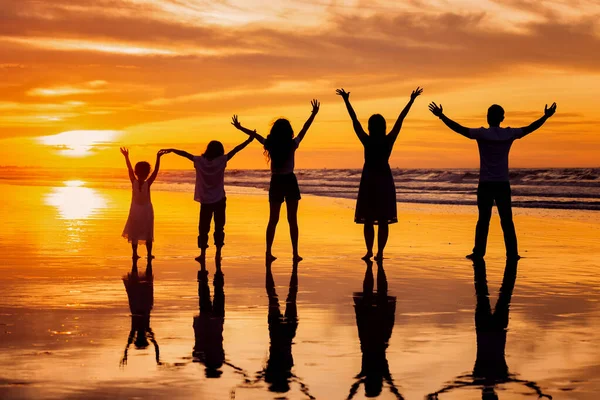 back view silhouette of happy family holding hands up and having fun together on tropical beach at summer sunset