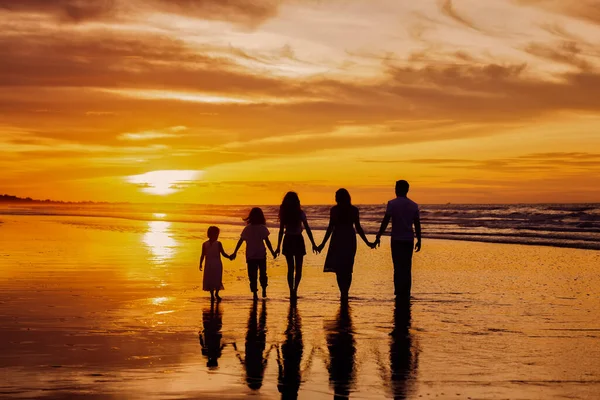 Silhouettes of big happy family holding the arms each other\'s on beach during golden sunset