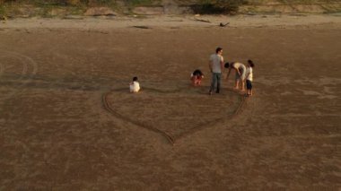 Büyük bir Asyalı ailenin havadan görünüşü kumda kalbi bir araya getirir. Aile, çocukluk ve tatil kavramı.