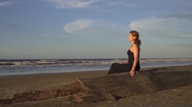 Gün batımında kumsalda tek başına oturan sakin kadın, nefes alıyor.