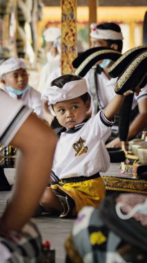 BALI, INDONESIA - April 2022: Cute small Balinese boy wearing traditional costume at traditional ceremony in Balinese temple, Indonesia
