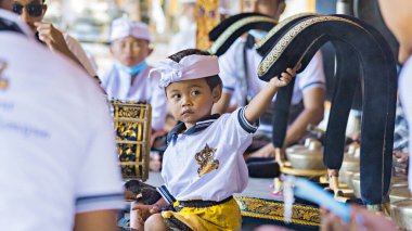BALI, INDONESIA - April 2022: Cute small Balinese boy wearing traditional costume at traditional ceremony in Balinese temple, Indonesia