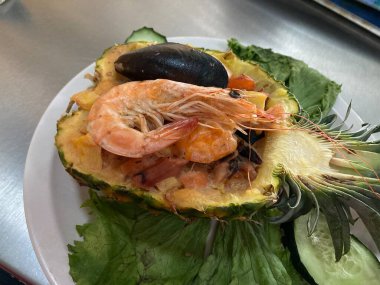 Ortada dilimlenmiş ananas tatlı salsa ve karidesle dolu ve deniz ürünleri lezzetli.