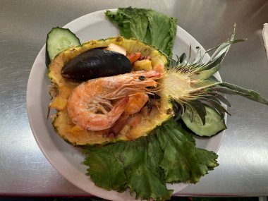 Ortada dilimlenmiş ananas tatlı salsa ve karidesle dolu ve deniz ürünleri lezzetli.