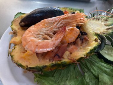 Ortada dilimlenmiş ananas tatlı salsa ve karidesle dolu ve deniz ürünleri lezzetli.