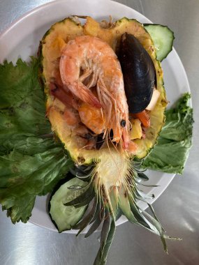 Ortada dilimlenmiş ananas tatlı salsa ve karidesle dolu ve deniz ürünleri lezzetli.