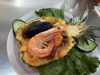 Ortada dilimlenmiş ananas tatlı salsa ve karidesle dolu ve deniz ürünleri lezzetli.