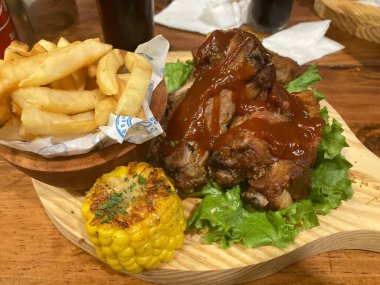 babyback ribs with bbq sauce , fried potatoes and a cub of corn