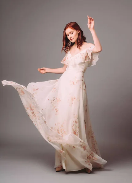 漂亮的年轻女子穿着白色晚礼服 花纹斑斑 穿着晚礼服 穿着灰色背景高跟鞋跳舞和跳舞的姜汁女郎的工作室肖像 — 图库照片