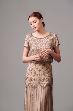 Zarif bej üzerine uzun bir elbise. Kızıl kadın stüdyoda poz veriyor. Kısa kollu, kahverengi boncuklu ve parlak pullu klasik gece elbisesi. Kadın cazibesi kıyafeti..