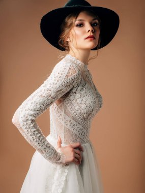 Kırsal gelinlik. Yumuşak pamuklu dantelli, uzun şeffaf kollu, gür tüllü etekli zarif gelinlik. Siyah kovboy şapkası tedarikli güzel sarışın gelin. Stüdyo çekimi.