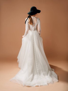 Kırsal gelinlik. Yumuşak pamuk dantelli zarif gelinlik, uzun şeffaf kollu, trenli tüllü etek. Siyah kovboy şapkası tedarikli güzel sarışın gelin. Stüdyo çekimi.