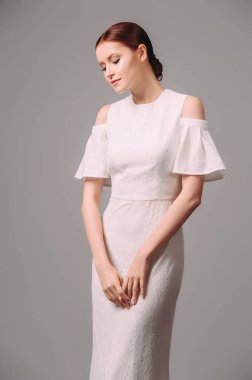 Modern gelin görünüşü. Beyaz gelinlikli güzel kızıl gelin. Omuzlarından ve boyunlarından çiçek desenli uzun trompet elbisesi. Stüdyo çekimi.