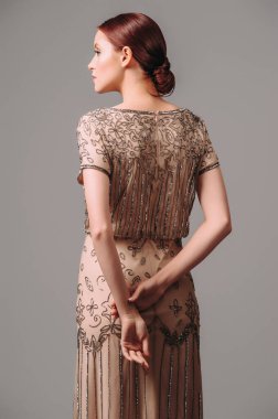 Elegant beige fitted long gown. Ginger lady posing in studio. Full length evening dress in vintage style with short sleeves and brown shiny beads. Female glamour outfit.