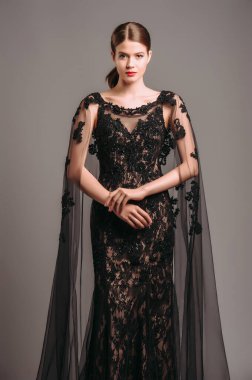 Şeffaf pelerinli, siyah, dantelli bir gece elbisesi. Trenle nakışlı Maxi elbise, modern moda. Balıkkuyruklu elbise. Esmer model stüdyoda poz veriyor. Tamamen siyah kadın görünüşü.. 