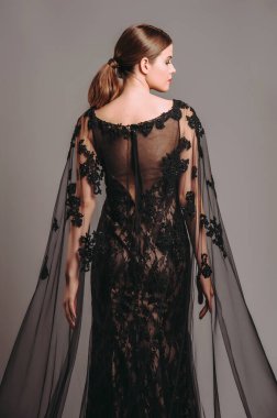 Şeffaf pelerinli, siyah, dantelli bir gece elbisesi. Trenle nakışlı Maxi elbise, modern moda. Balıkkuyruklu elbise. Esmer model stüdyoda poz veriyor. Tamamen siyah kadın görünüşü.. 