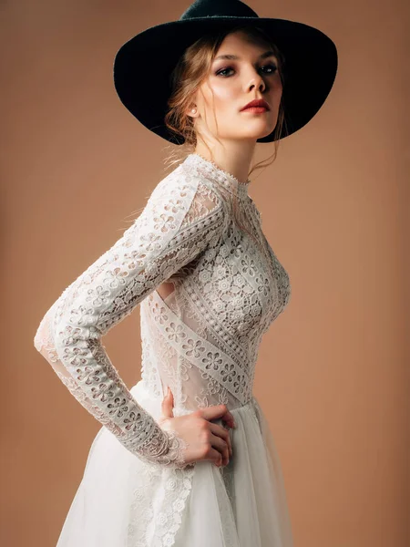 Kırsal gelinlik. Yumuşak pamuklu dantelli, uzun şeffaf kollu, gür tüllü etekli zarif gelinlik. Siyah kovboy şapkası tedarikli güzel sarışın gelin. Stüdyo çekimi.