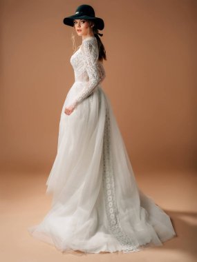 Kırsal gelinlik. Yumuşak pamuk dantelli zarif gelinlik, uzun şeffaf kollu, trenli tüllü etek. Siyah kovboy şapkası tedarikli güzel sarışın gelin. Stüdyo çekimi.