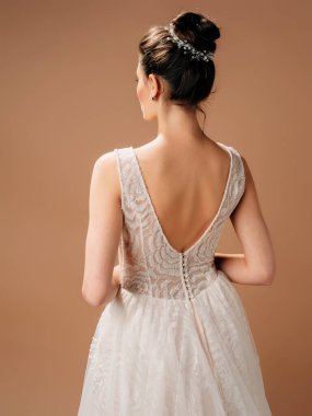 Backless wedding dress. Gorgeous sleeveless bridal gown with tender french lace and beads, long lush tulle skirt. Beautiful brunette lady bride with bun hairstyle. Studio shot on powder background. clipart