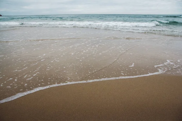 Ocean waves on a sandy beach with cloudy skies — Stock Photo, Image
